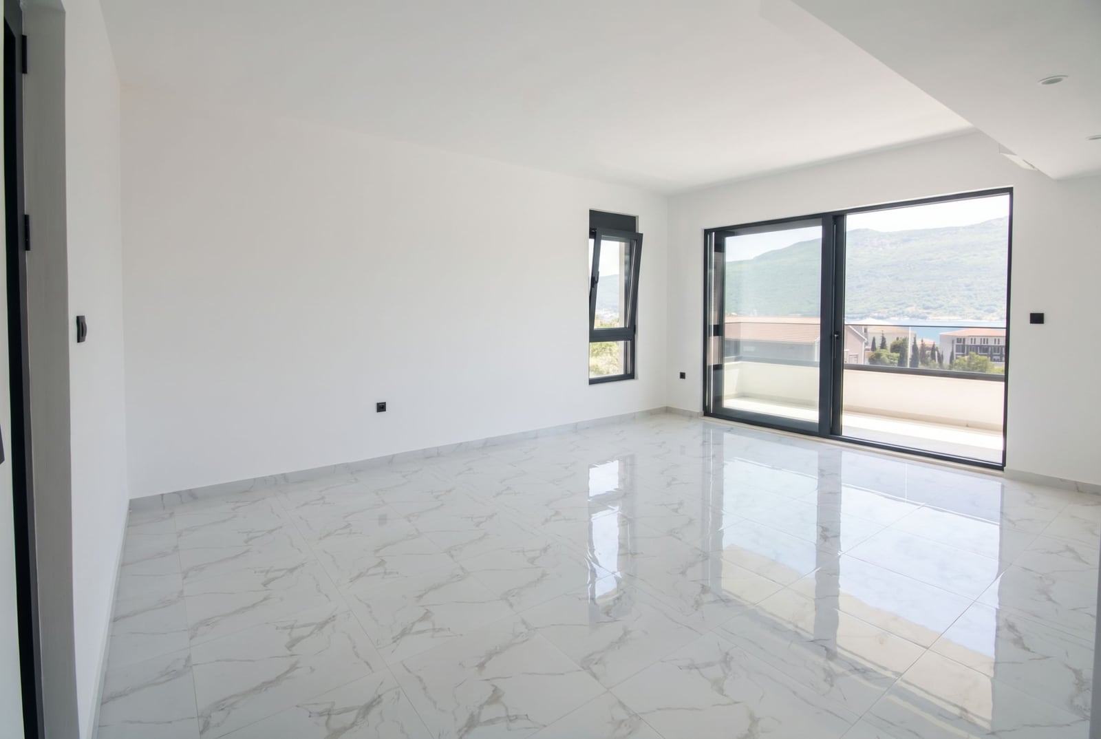 Bright living room in a new apartment in Kumbor, Montenegro: marble floor, panoramic windows with sea and mountain views.