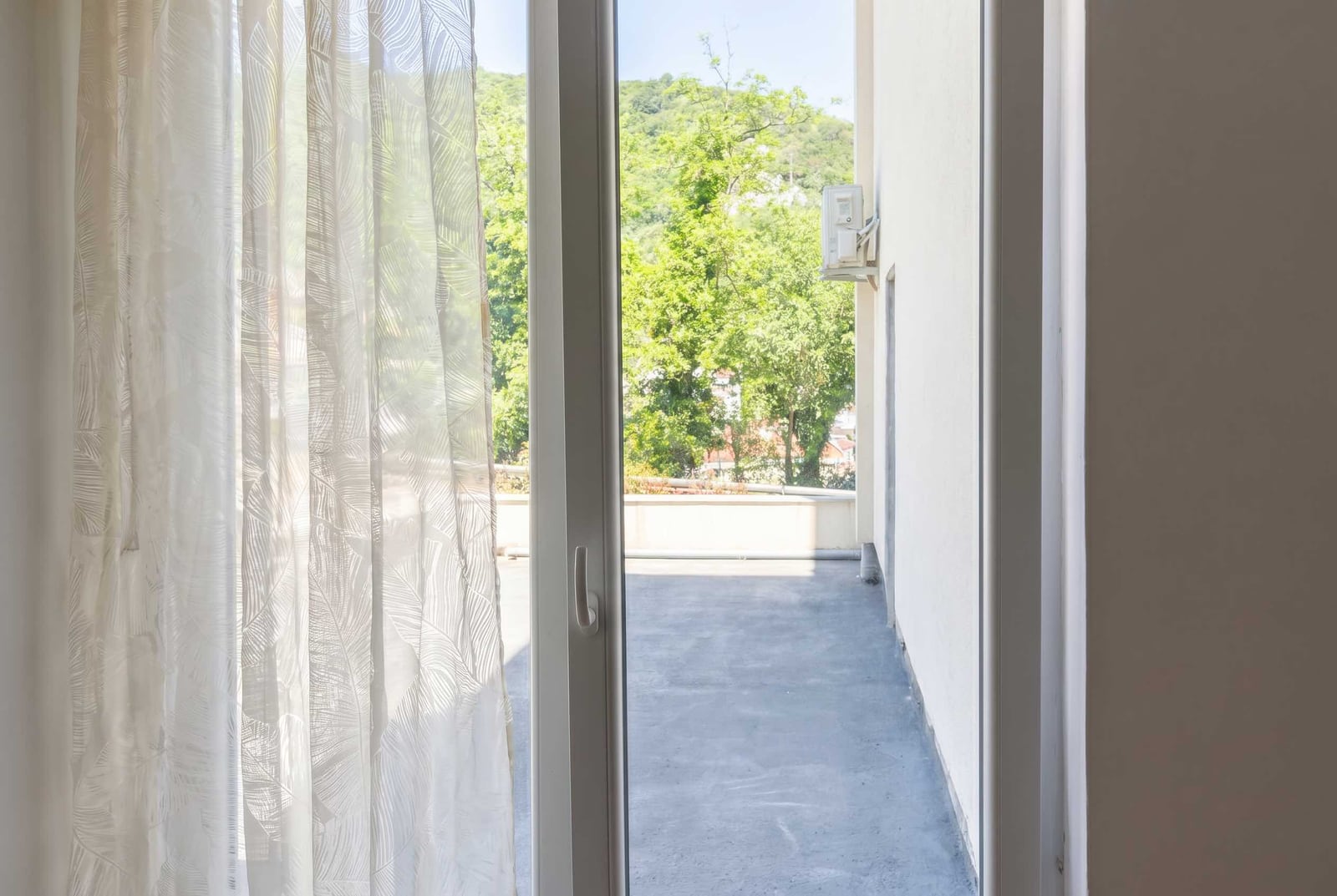 View from the balcony of an apartment in Budva, Montenegro: an open terrace with a green mountain landscape and a bright interior.