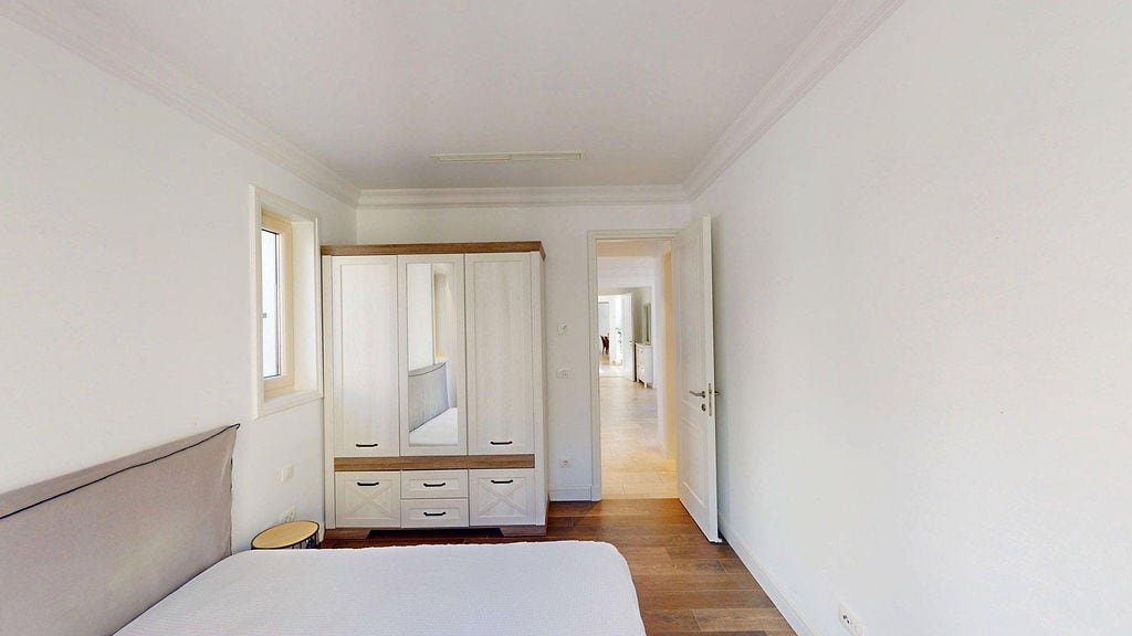 Bright bedroom with a white wardrobe and bed in an apartment in Luštica, Montenegro. Modern interior with wooden flooring.