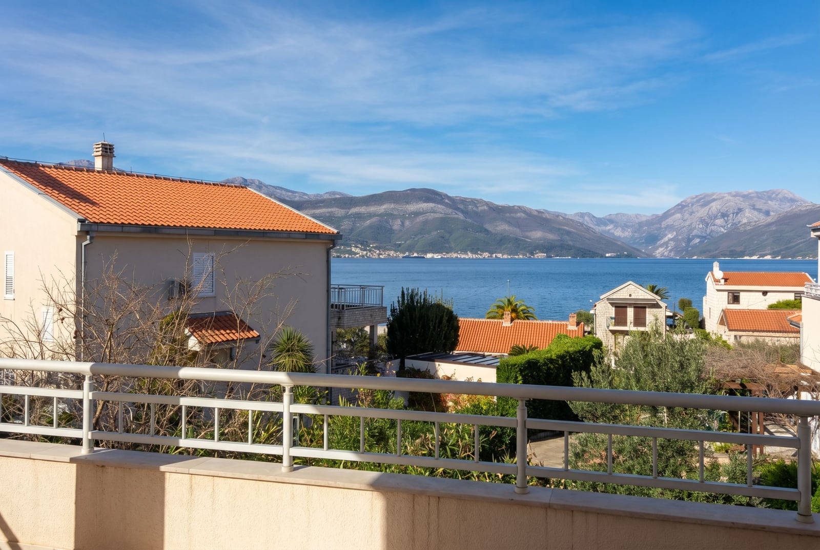 View from the balcony of a house in Baošići, Montenegro: a panorama of the sea, mountains, and tiled roofs on a sunny day.