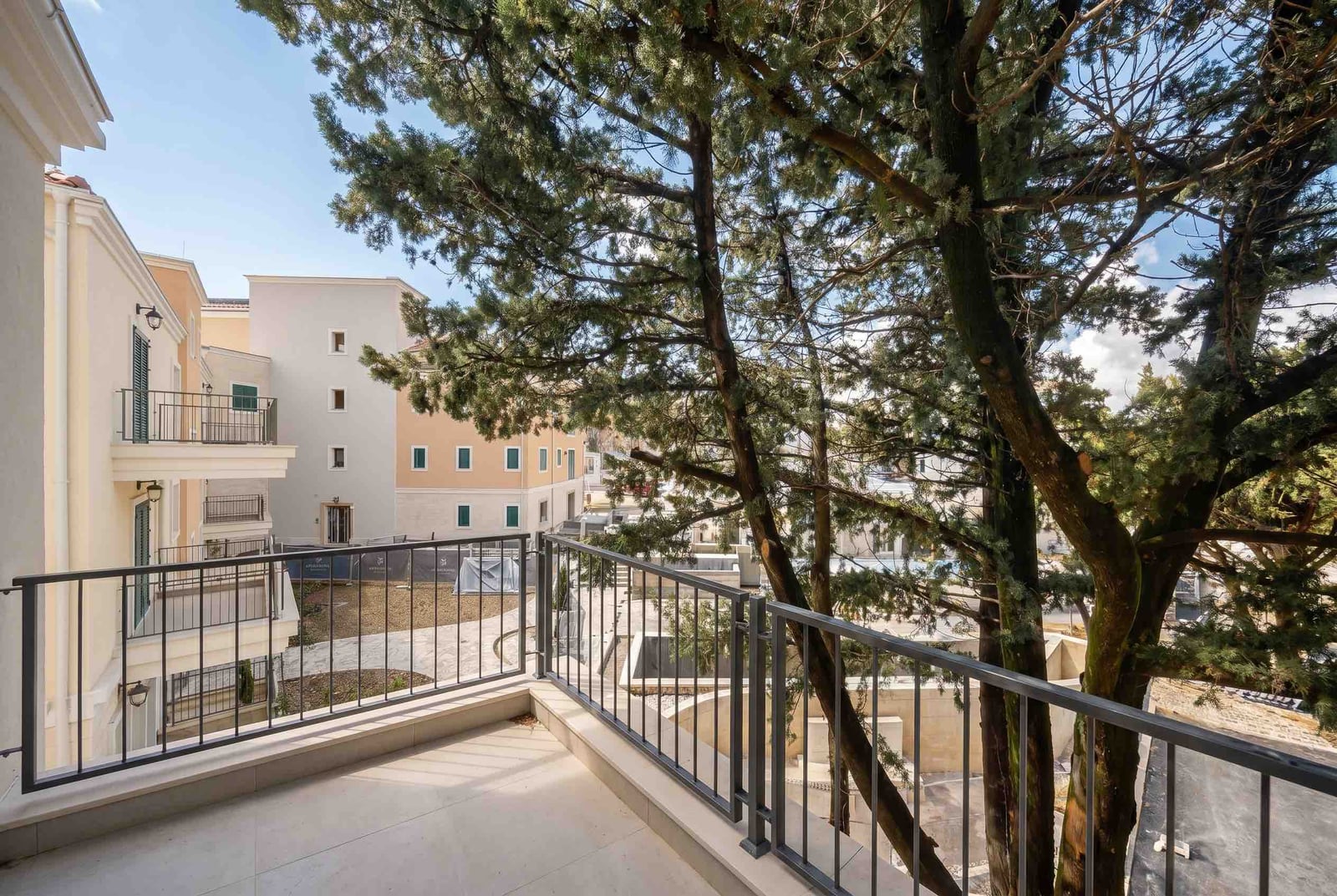 View from the balcony of a modern apartment in Luštica, Montenegro: a terrace with railing and a panorama of the residential complex with trees.