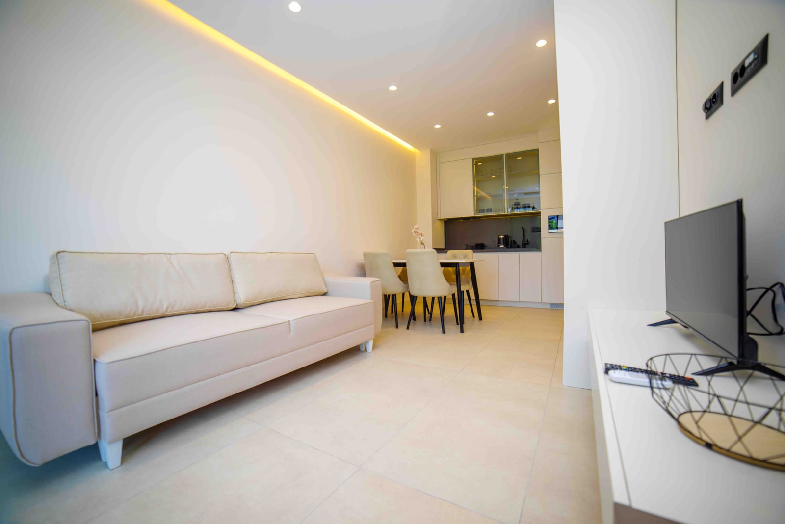 Modern living room with kitchen in an apartment in Bečići, Montenegro: light-colored sofa, dining area, and built-in furniture.