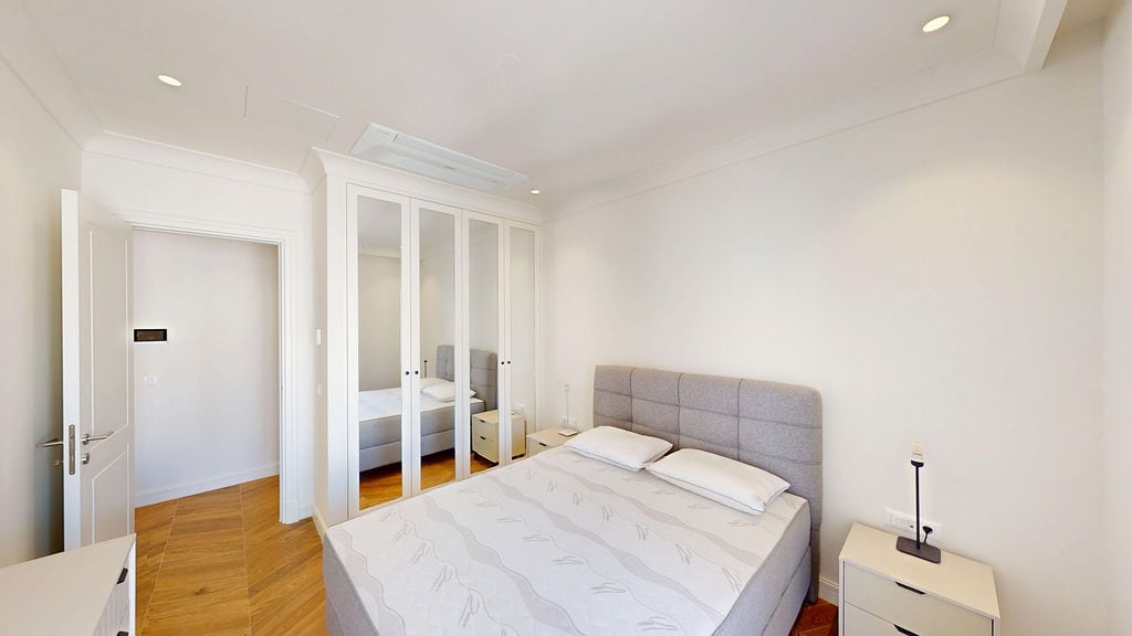 Modern bedroom in a Lustica Bay apartment, Montenegro: double bed, built-in mirrored wardrobe, and light interior.