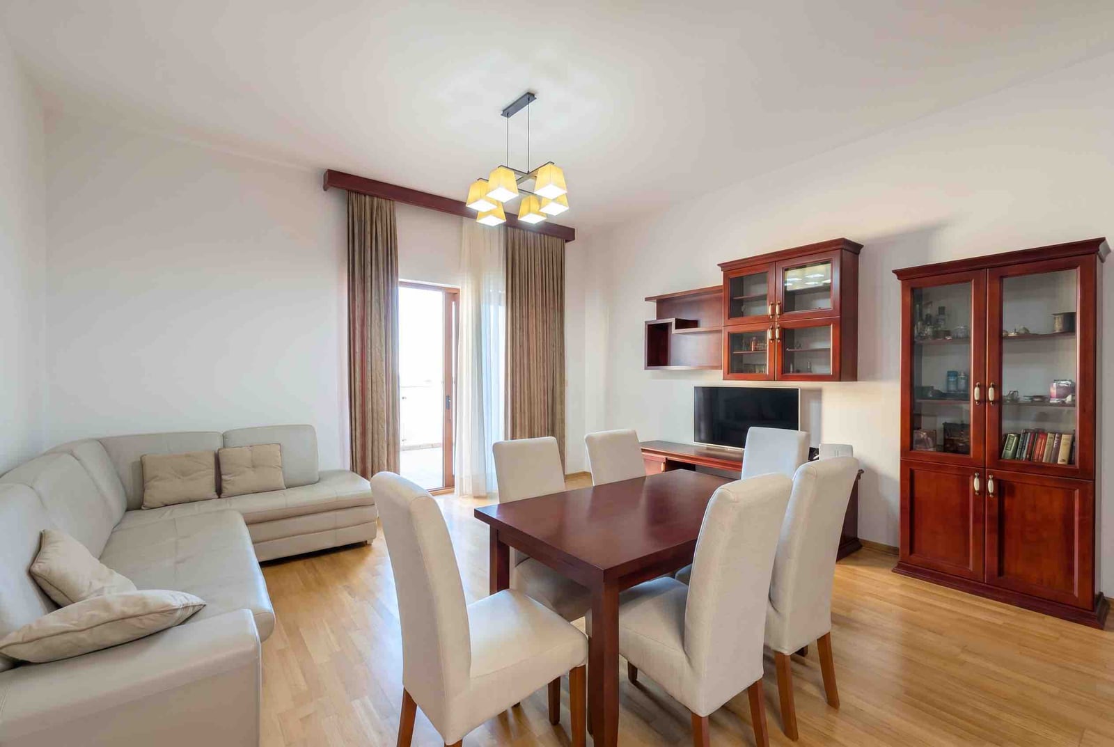 Living room with dining area and light-colored furniture in an apartment, Bečići residential complex, Montenegro: interior with a wooden table and cabinet.