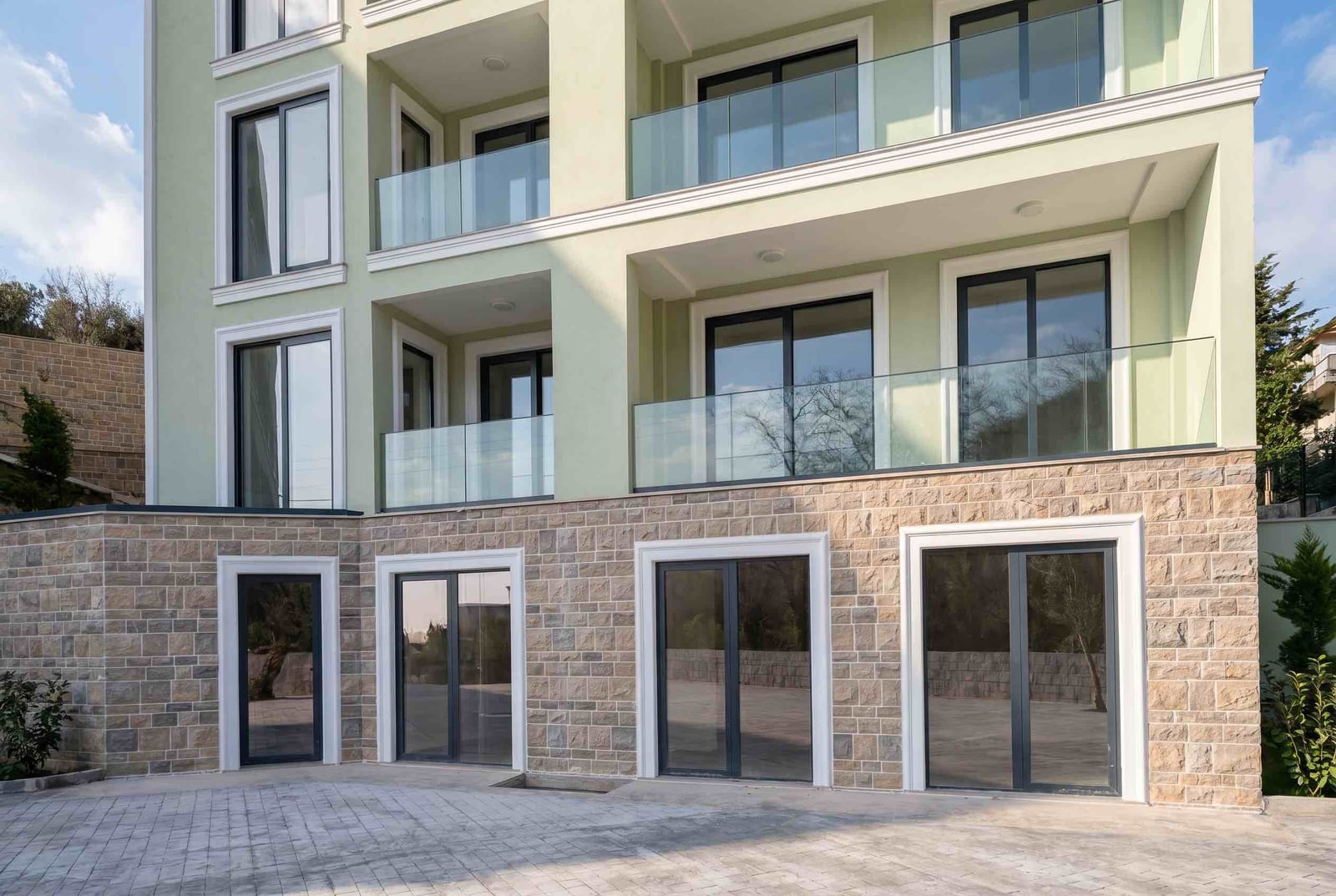Facade of a modern residential building in Pržno, Montenegro: stone cladding, panoramic windows, and glass balconies of the apartments.