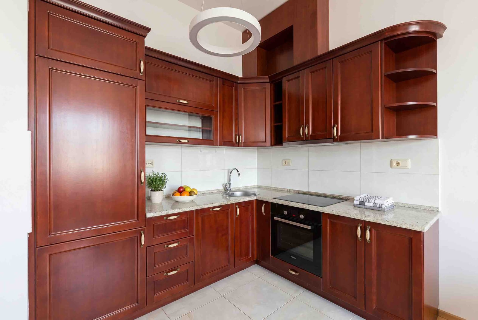 Corner kitchen made of dark wood with a light countertop in an apartment at the Bečići residential complex, Montenegro. Modern household appliances.