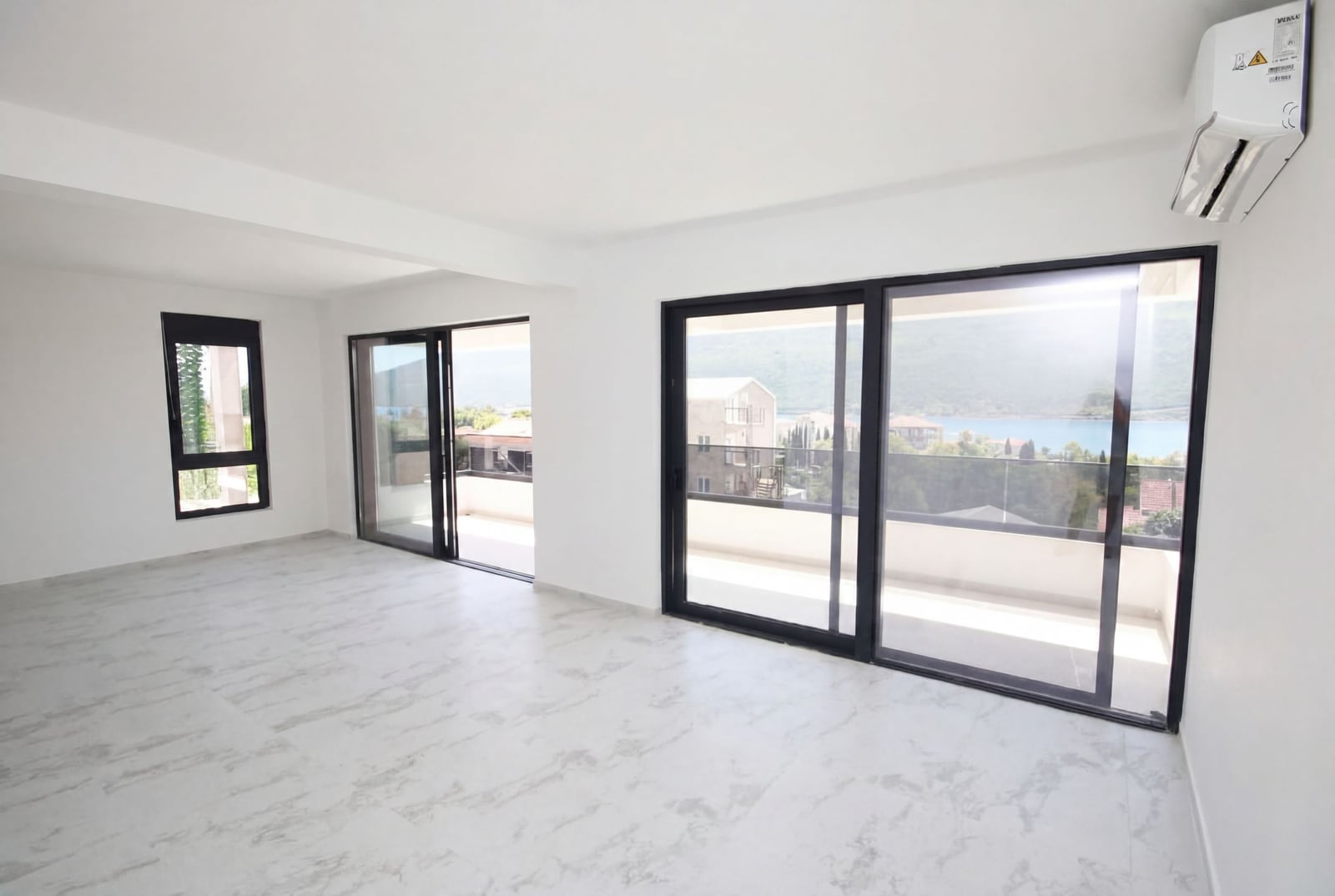 Bright living room in an apartment in Kumbor, Montenegro, with panoramic windows, access to the terrace, and sea view.