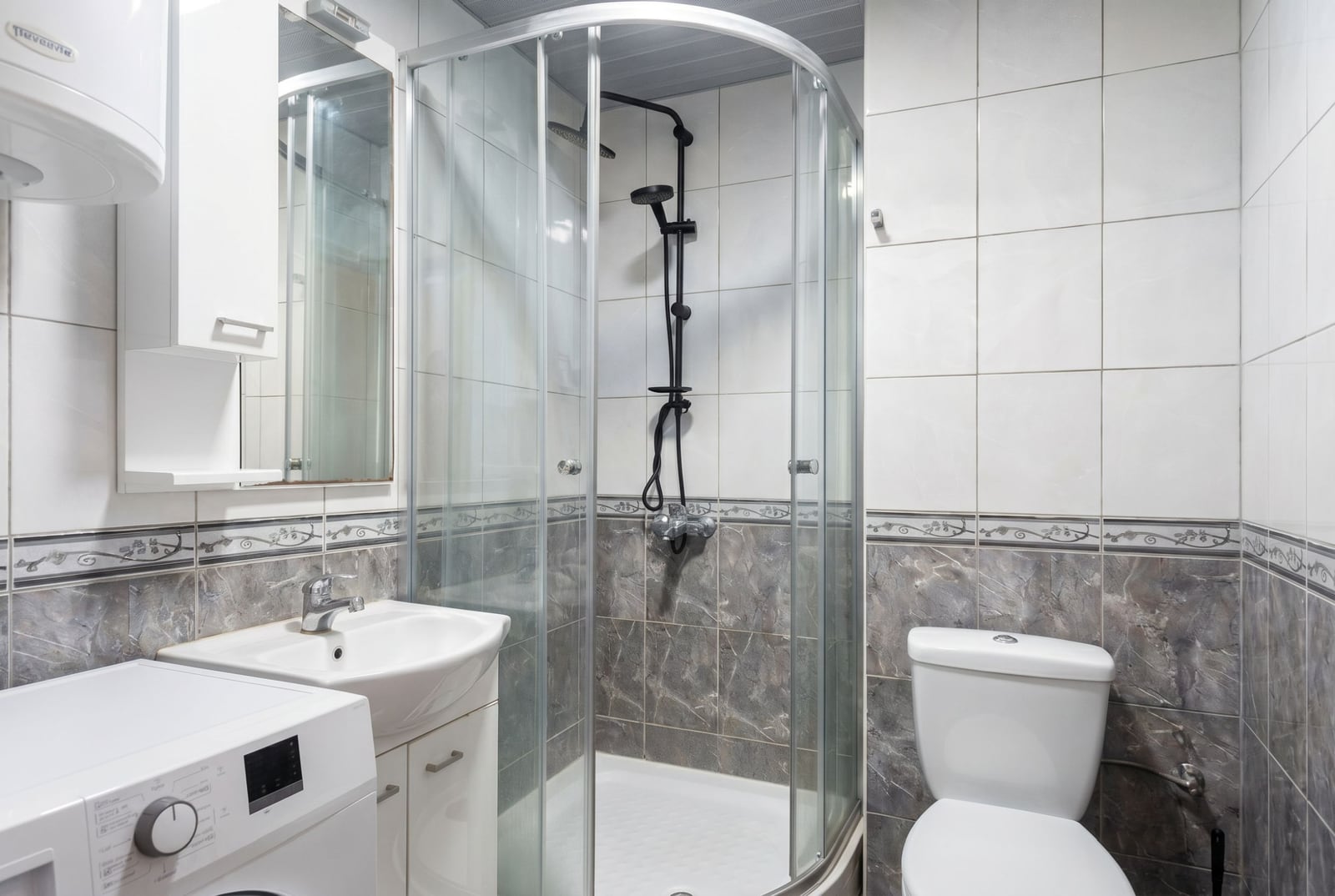 Bathroom in an apartment in Budva, Montenegro: shower cabin, sink with vanity, toilet, and washing machine.