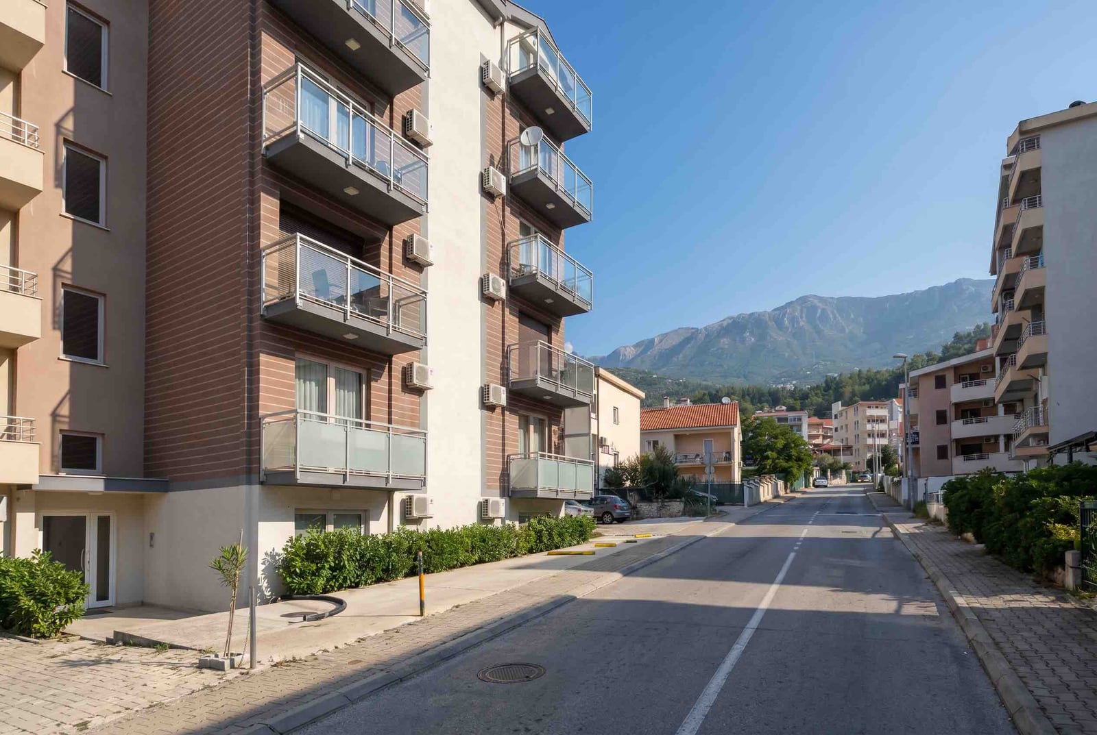 Modern residential building with balconies in Budva, Montenegro, street view and mountain landscape on a sunny day.