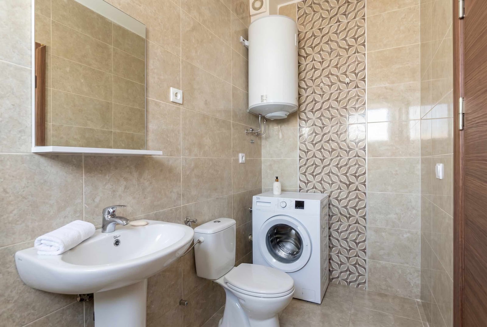 Modern bathroom in an apartment, Budva, Montenegro: light-colored tiles, plumbing fixtures, water heater, and washing machine.