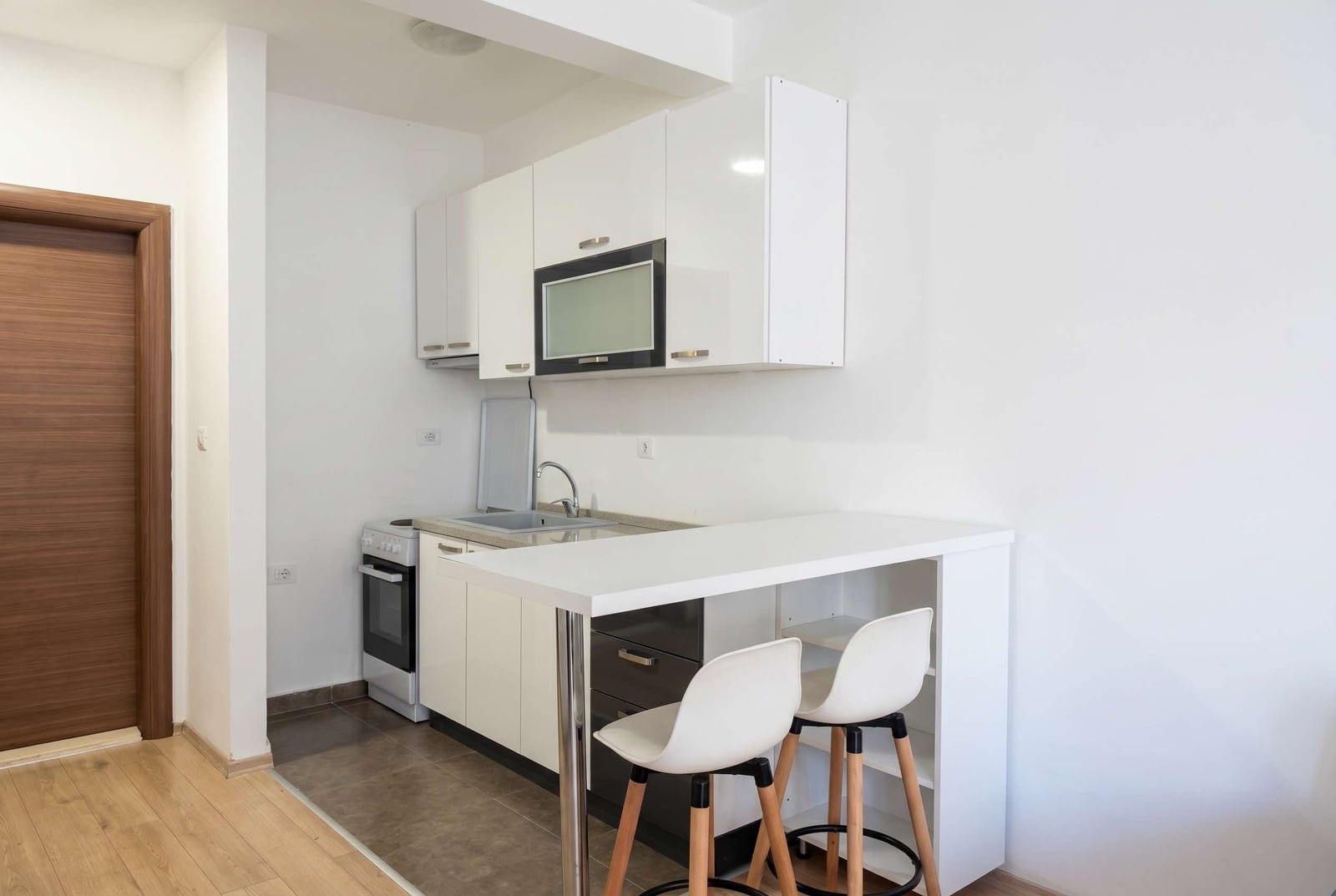 Modern white kitchen with a bar counter and stools in an apartment in Budva, Montenegro. Compact cooking area.