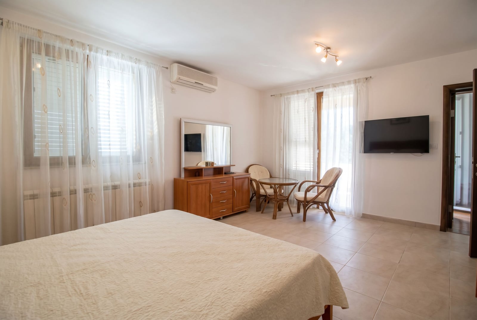 Bright bedroom with a double bed and sitting area in a house in Baošići, Montenegro: wooden furniture, TV, and balcony.