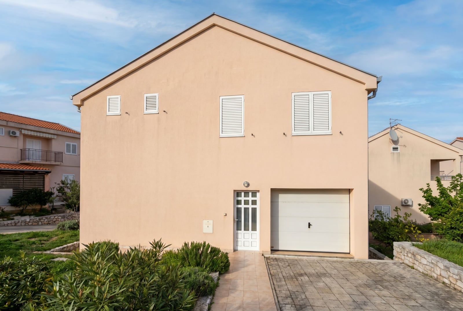Two-story house in Baošići, Montenegro: beige facade, garage, front door, and landscaped grounds.