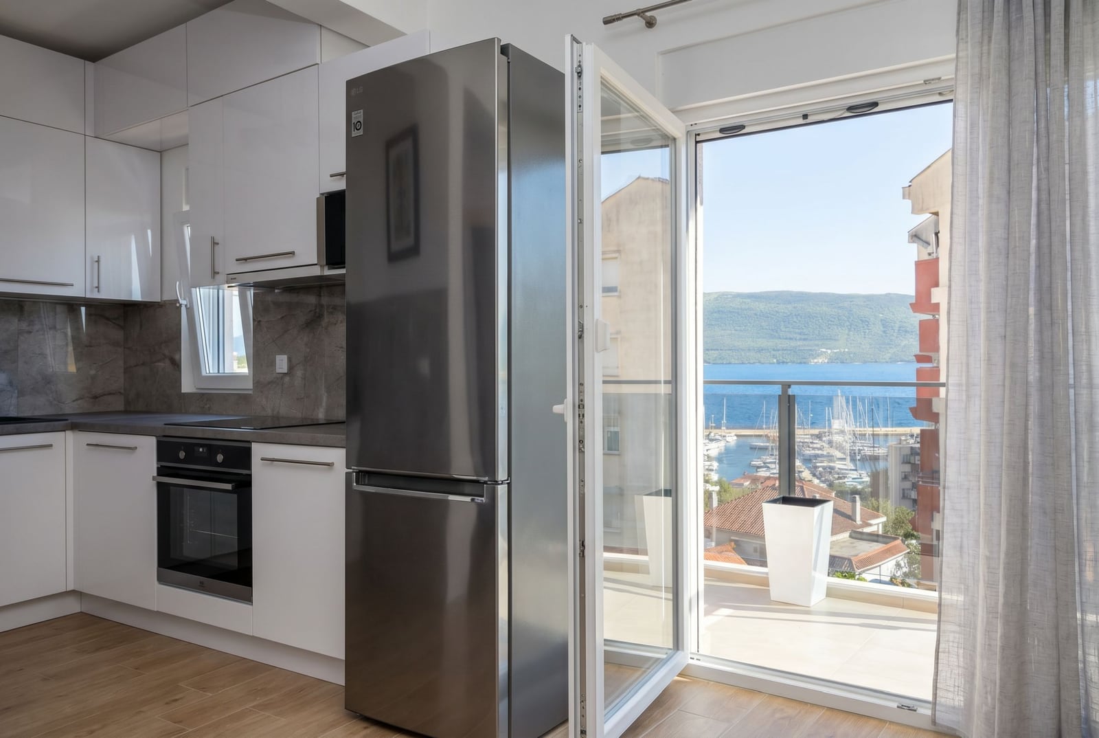 Modern kitchen in an apartment, Herceg Novi, Montenegro: white cabinetry, sea view and yacht marina from the balcony.
