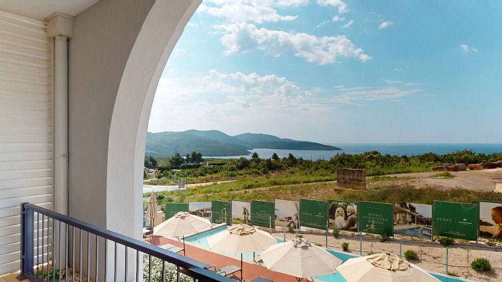 View from the balcony of an apartment in Luštica, Montenegro: pool with umbrellas, panorama of mountains and the Adriatic Sea.