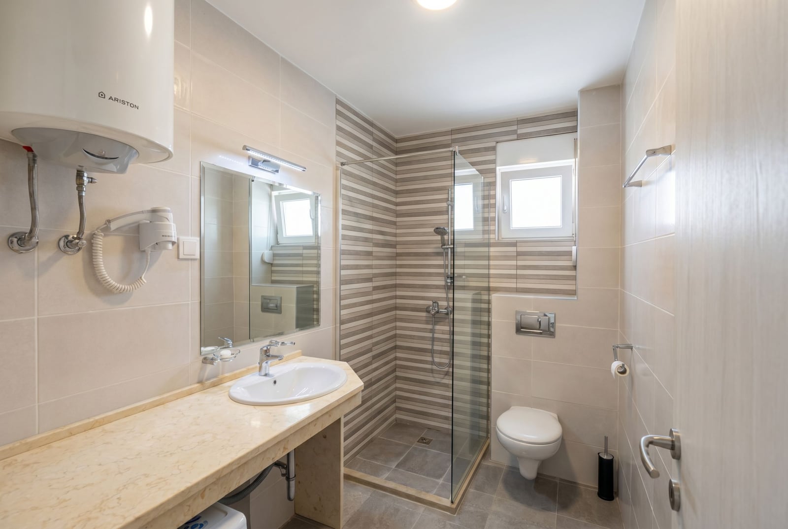 Modern bathroom in an apartment in Budva, Montenegro: shower cabin, light tiles, and a stone countertop.