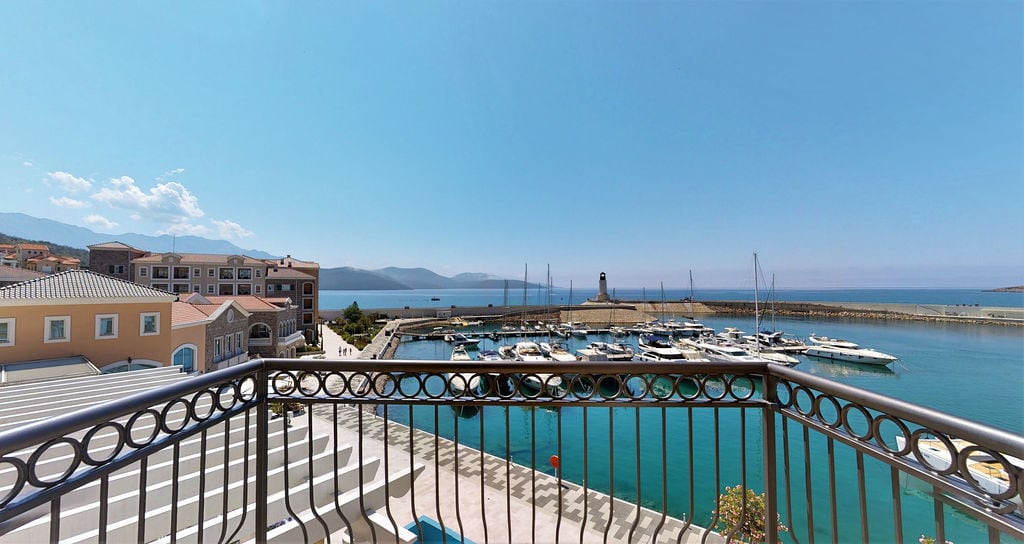 View from the balcony overlooking the marina and yachts at the Luštica Bay residential complex, Montenegro: a panorama of the sea and mountains on a sunny day.