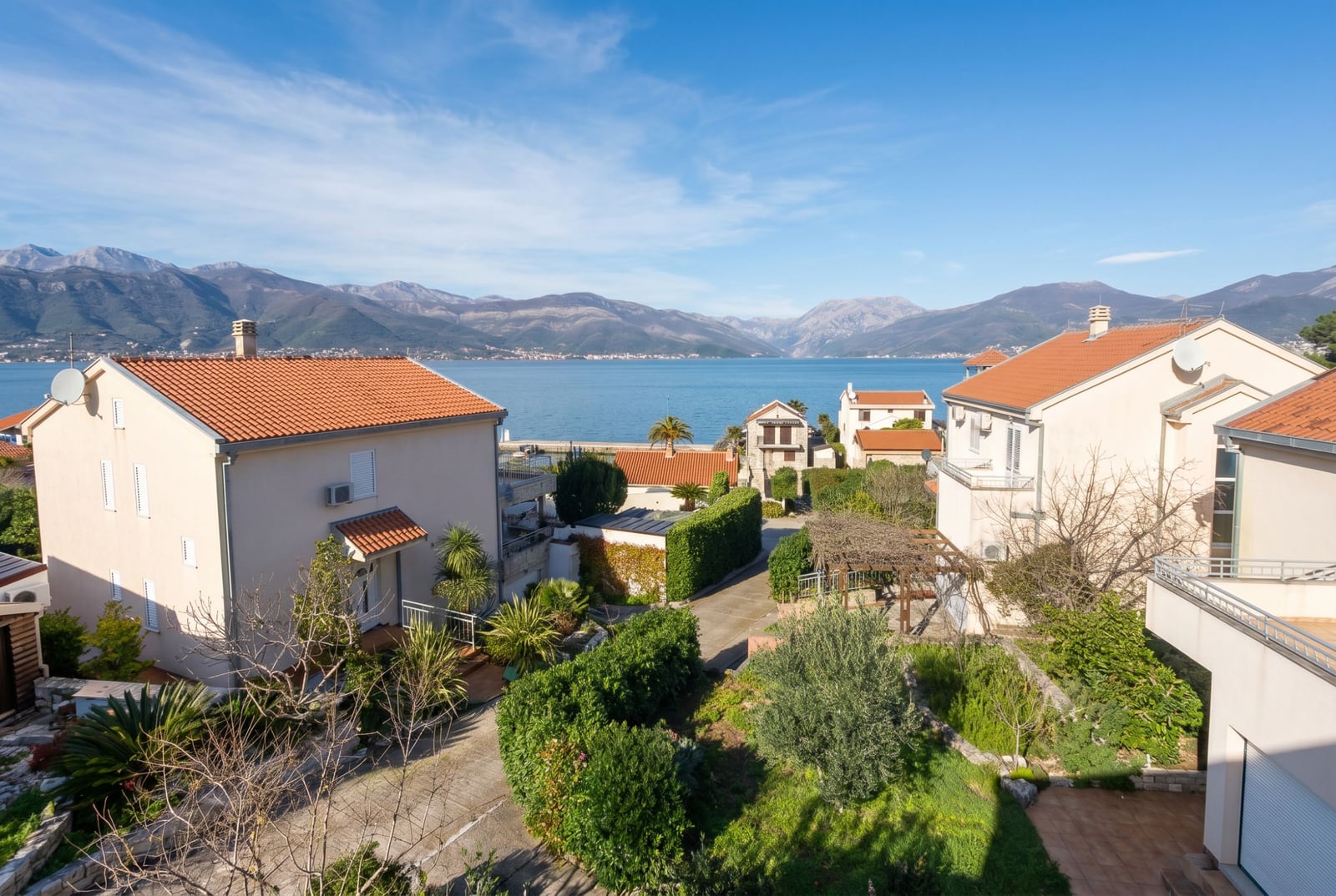 Sea and mountain view from a house in Baošići, Montenegro: a cozy garden area and cottages with tiled roofs.