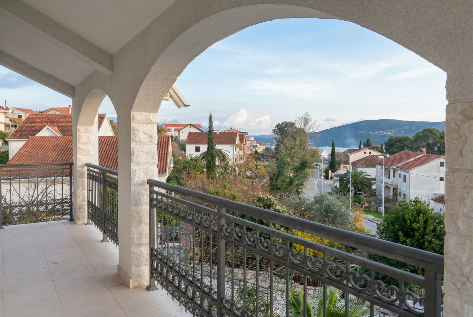 View from the arched balcony of a house in Herceg Novi, Montenegro: wrought-iron railings, tiled floor, and a panoramic view of the city and the sea.