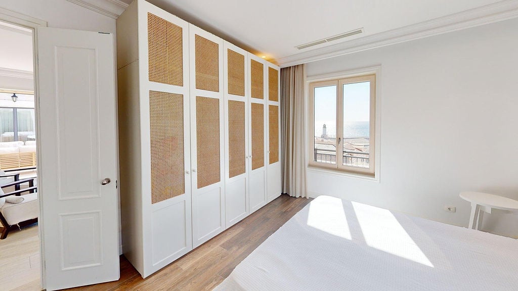 Bedroom in an apartment, Luštica, Montenegro: white wardrobe with rattan inserts, light interior, and a sea view from the window.