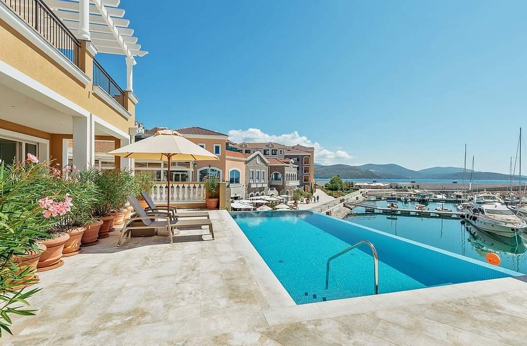 Pool with a view of the marina and yachts at the Luštica Bay residential complex, Montenegro: terrace with sun loungers and an umbrella.