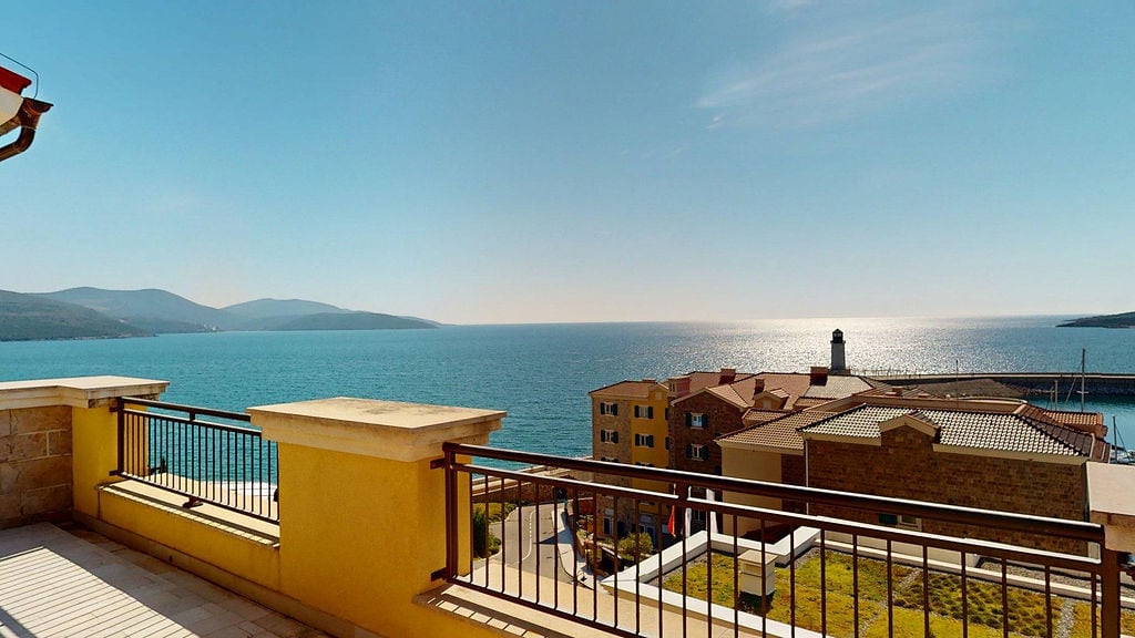 View from the balcony overlooking the sea and the lighthouse in the Luštica Bay residential complex, Montenegro: a terrace with railing and panoramic scenery.