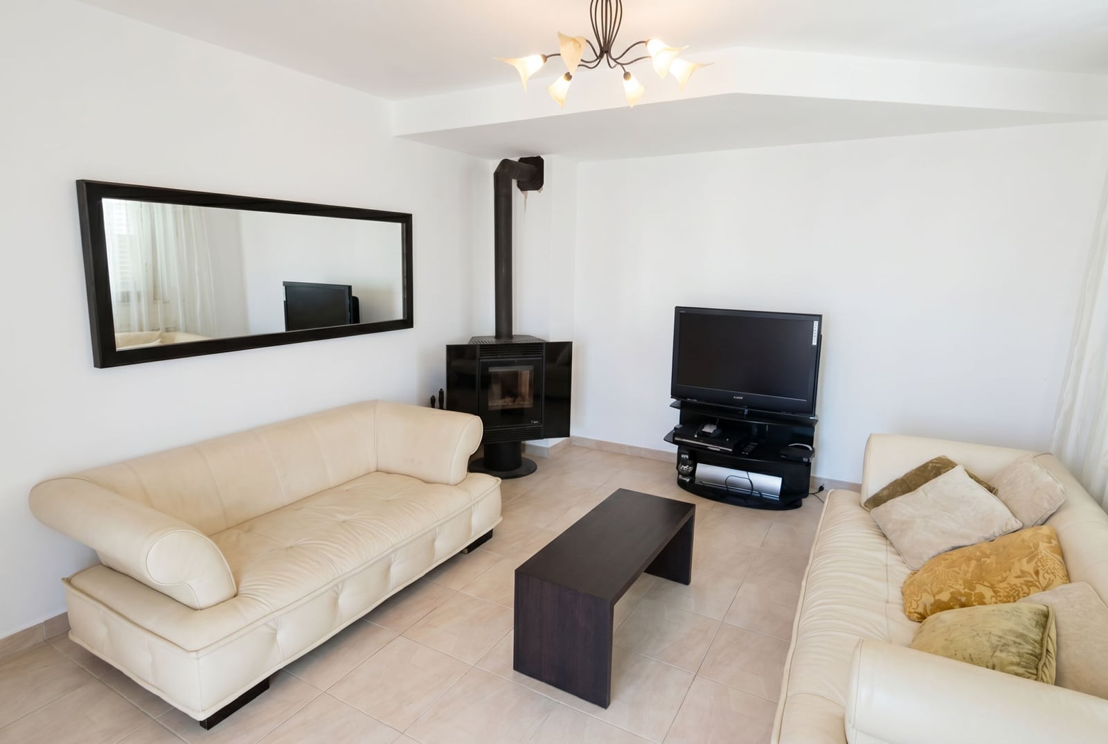 Living room in a house in Baošići, Montenegro: light leather sofas, a fireplace, TV area, and a mirror in a modern interior.