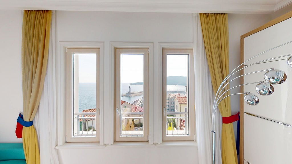 Sea view and lighthouse from the living room window in an apartment, Krašići, Montenegro: bright interior with yellow curtains.