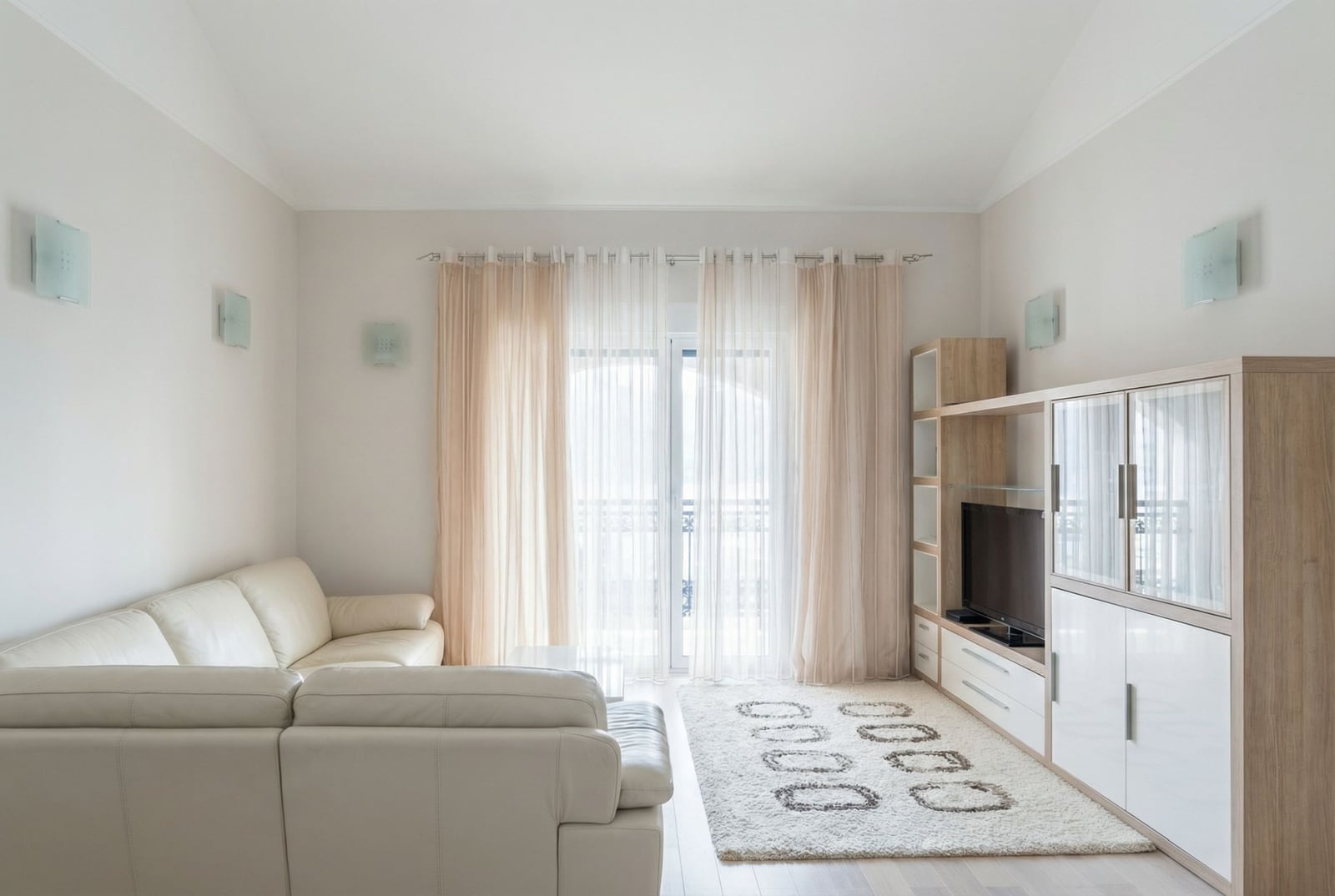 Bright living room in a house in Herceg Novi, Montenegro: white leather sofa, modern wall unit, and access to the balcony.