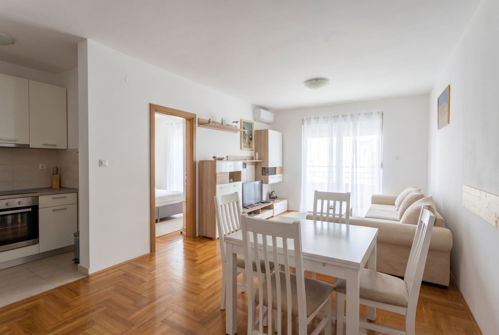 Bright living room with kitchen in an apartment, Budva, Montenegro: white furniture, parquet floor, and access to the balcony.