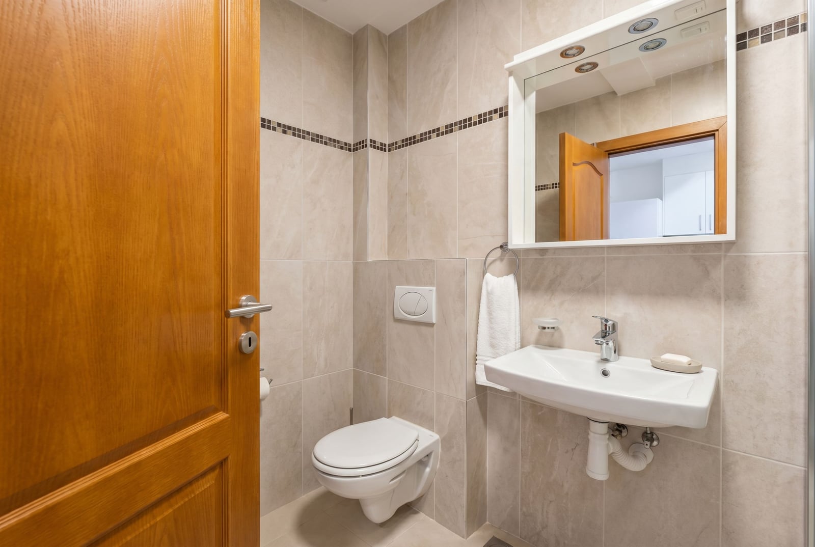 Modern bathroom in an apartment, Herceg Novi, Montenegro: beige tiles, wall-mounted toilet, and a sink with mirror.