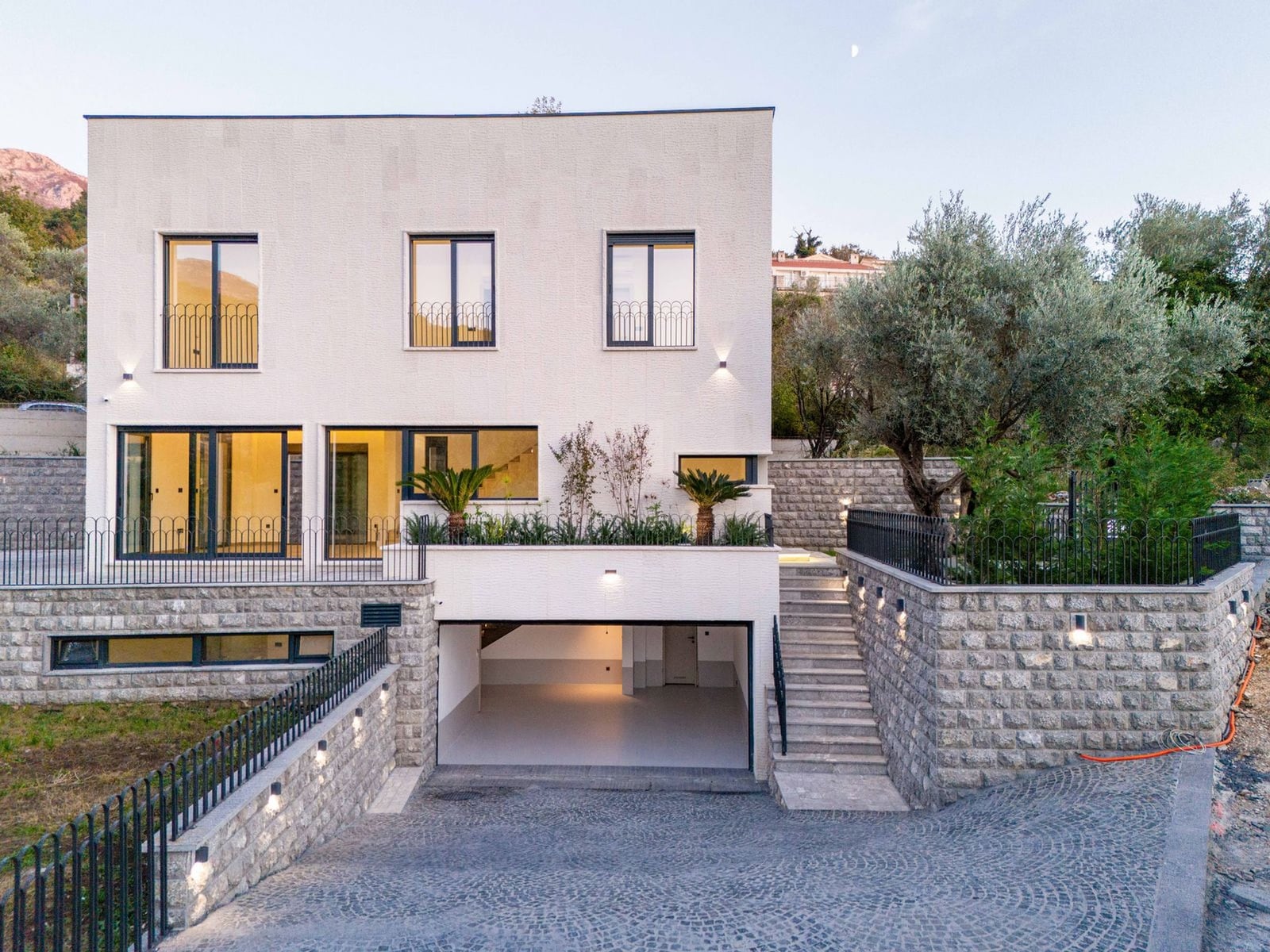 Villa moderne à Kamenovo, Monténégro : façade avec baies panoramiques, terrasse, aménagement paysager et garage.