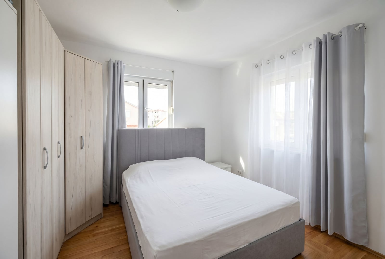 Bright bedroom with a double bed and wardrobe in an apartment, Budva, Montenegro. Modern interior with parquet flooring.