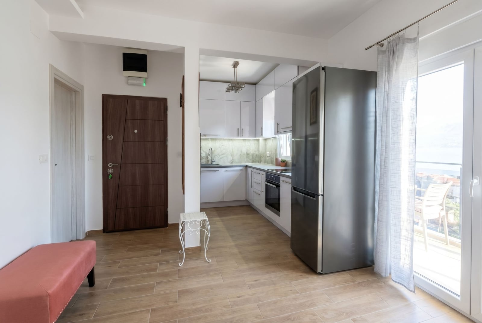 Modern kitchen in an apartment in Herceg Novi, Montenegro: white cabinetry, built-in appliances, and access to a balcony with a view.