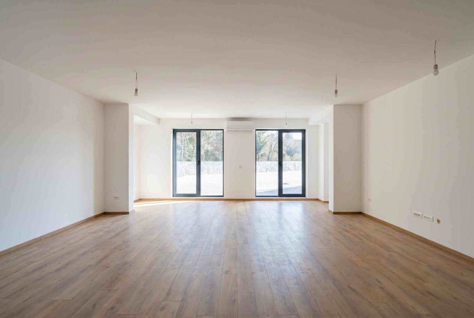 Bright living room in an apartment in Pržno, Montenegro: laminate flooring, white walls, panoramic windows, and a view of greenery.