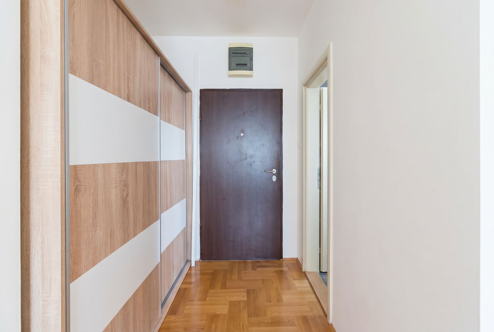 Hallway in an apartment in Bečići, Montenegro: built-in sliding wardrobe, parquet floor, and an entrance door in a bright interior.