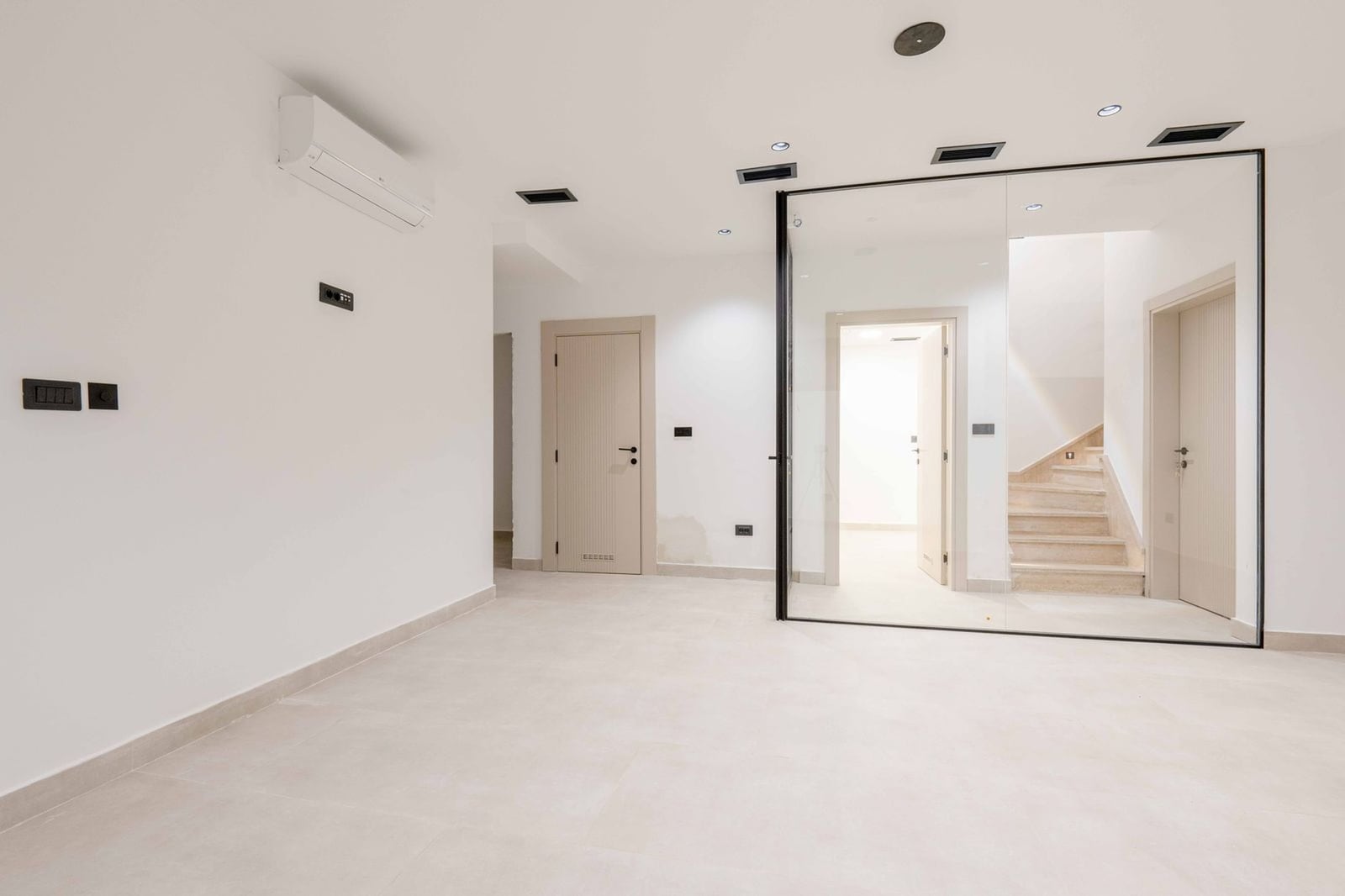 Salon moderne avec finitions blanches, cloison vitrée et escalier dans une villa à Kamenovo, Monténégro.