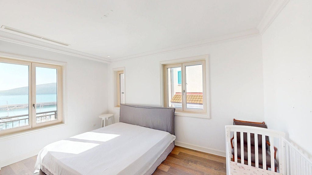Bright bedroom with a sea view in the Luštica residential complex, Montenegro: double bed, baby cot, and parquet flooring.