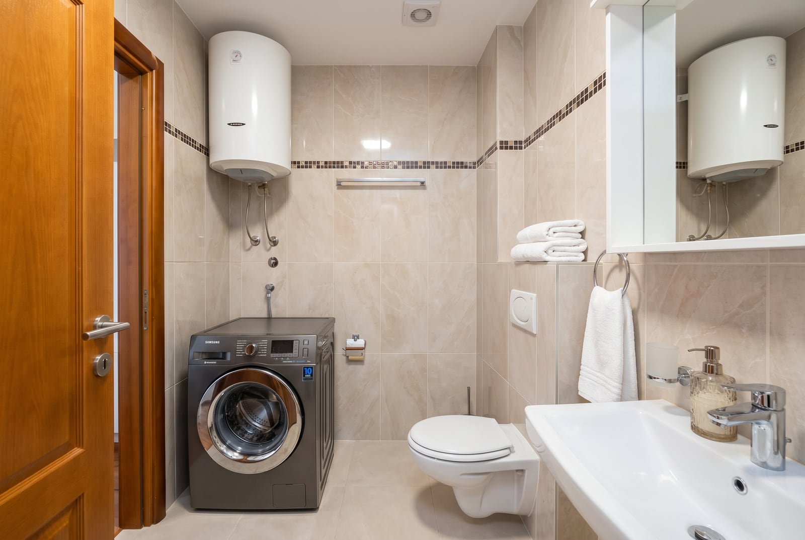 Bathroom in an apartment in Herceg Novi, Montenegro: beige tiles, wall-mounted toilet, and a gray washing machine.