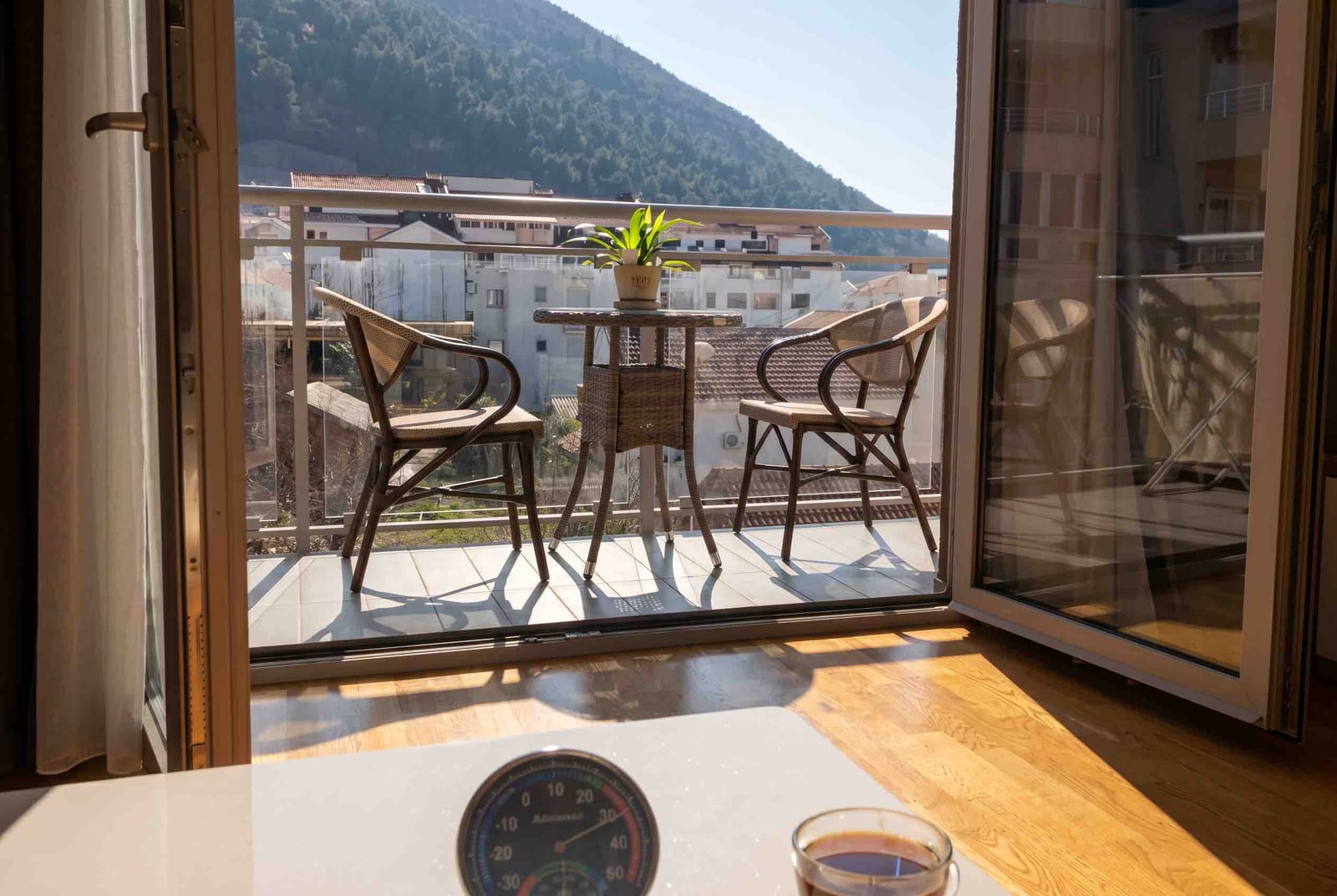Balcony with wicker furniture and mountain views in an apartment, Budva, Montenegro. Bright room with wooden flooring.