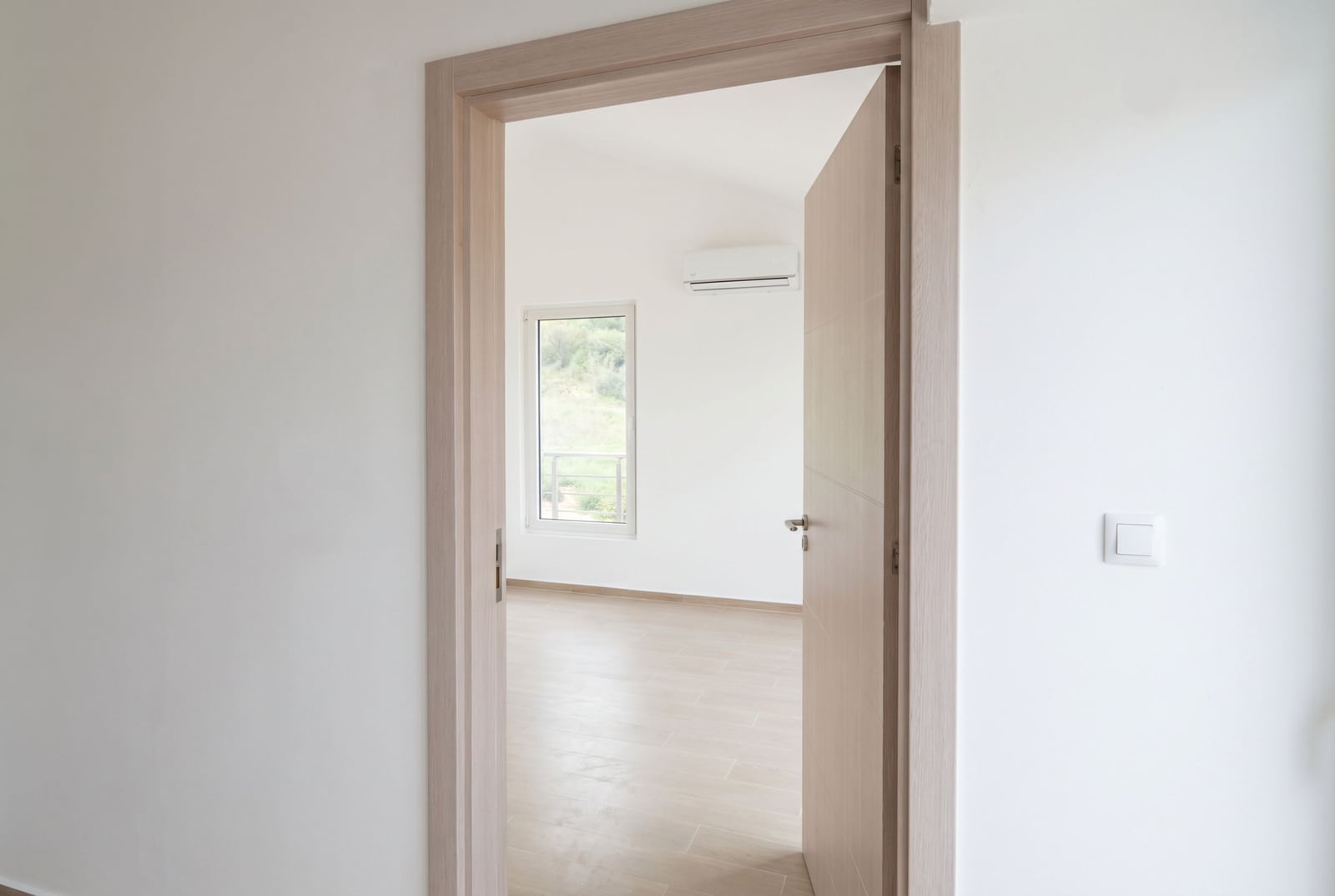 Bright bedroom in an apartment, Đenovići, Montenegro: interior door, white walls, air conditioner, and a view from the window.