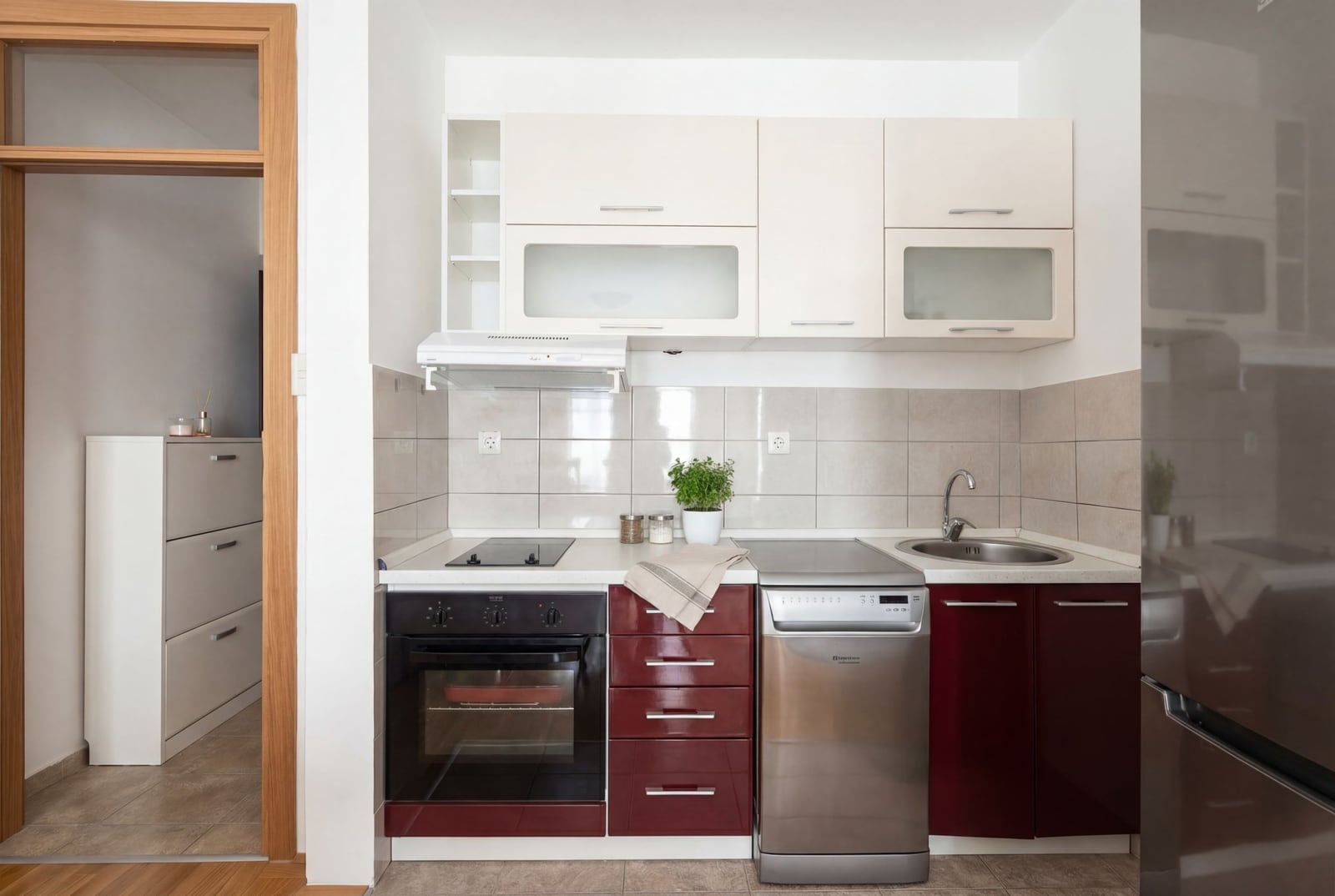 Modern kitchen in an apartment in Budva, Montenegro: built-in appliances, burgundy cabinet fronts, and light backsplash tiles.