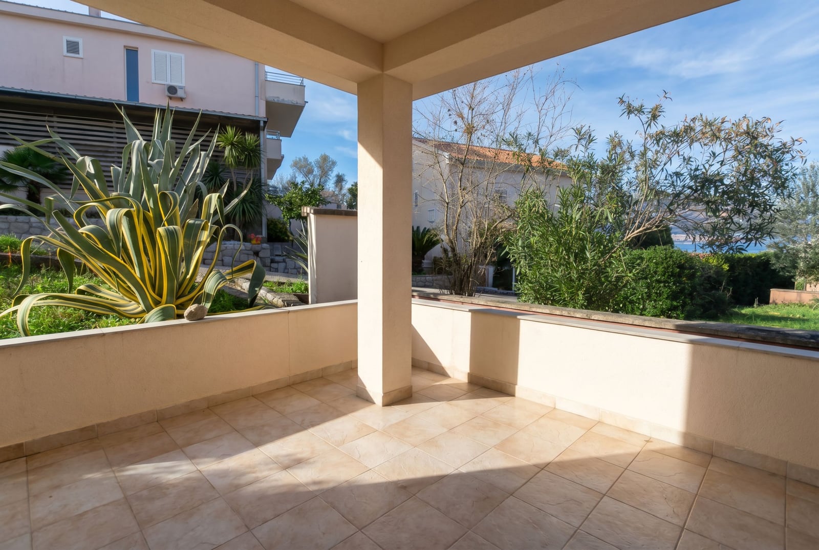 Spacious terrace with a view of the garden and the sea in a house, Baošići, Montenegro: tiled floor, agave, and Mediterranean greenery.