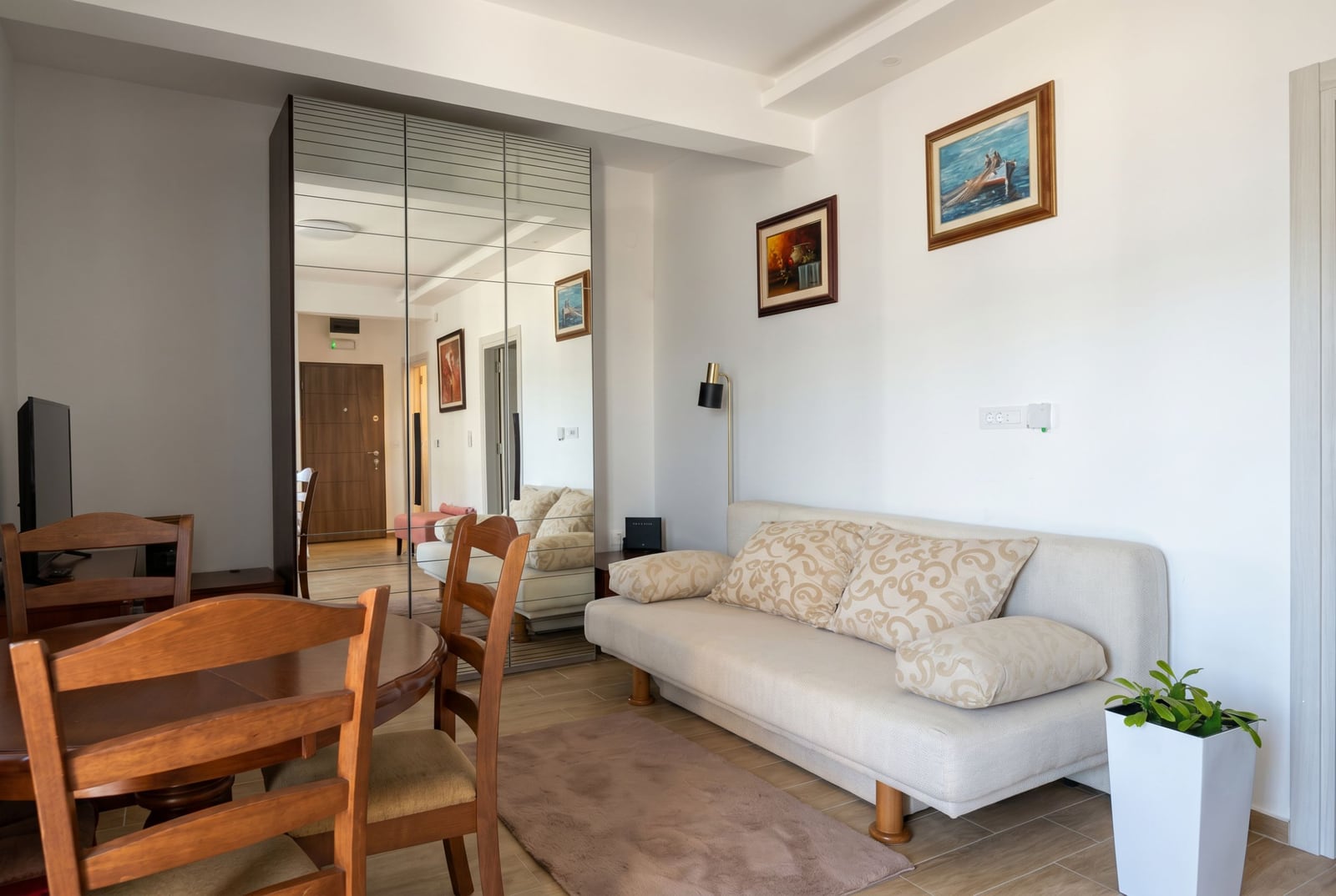Living room in an apartment in Herceg Novi, Montenegro: a light-colored sofa, mirrored sliding wardrobe, and a wooden dining area.