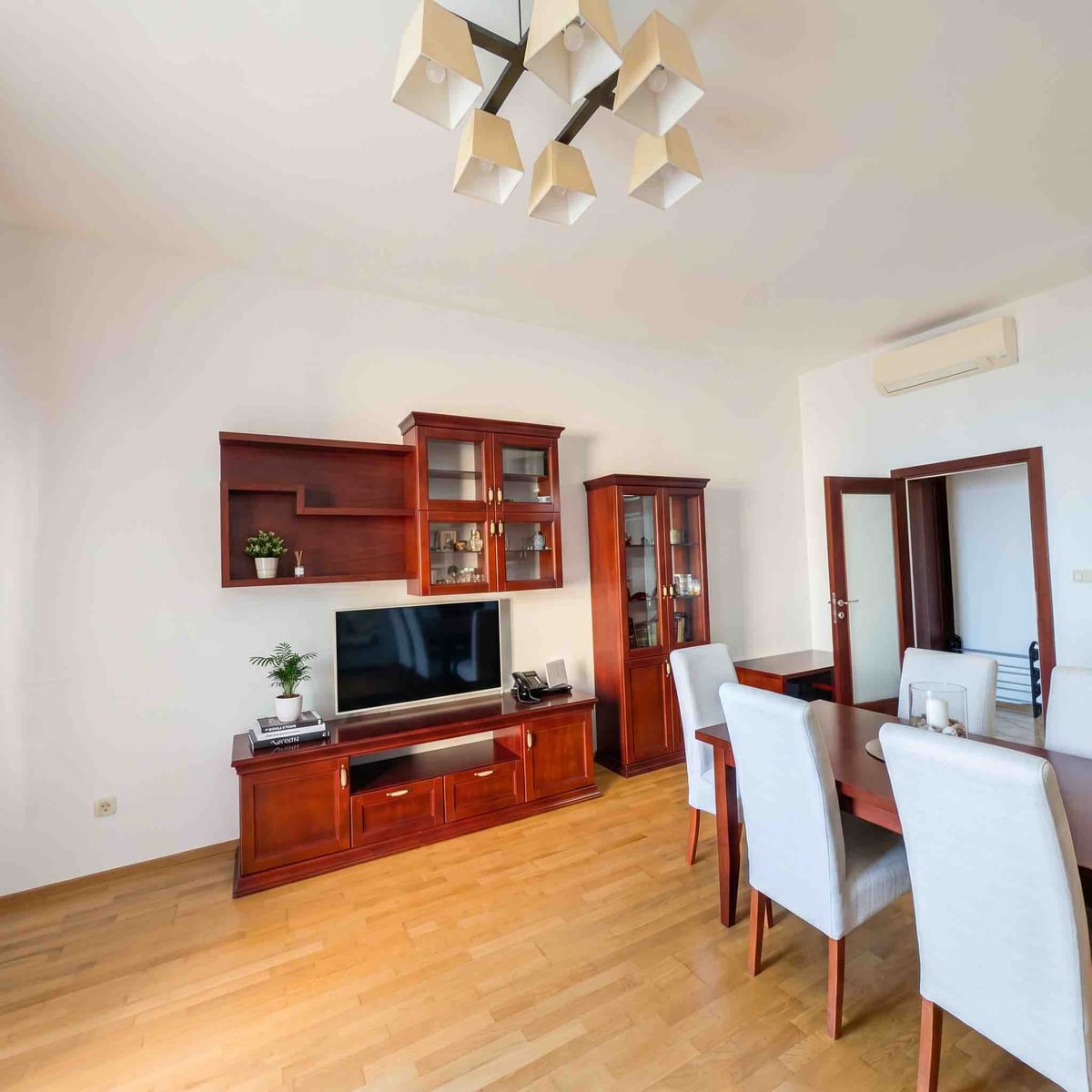 Living room with wooden furniture, dining area, and parquet flooring in an apartment in Bečići, Montenegro.