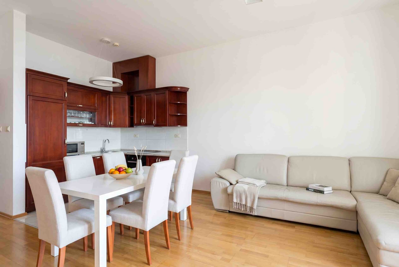 Modern living room with kitchen in an apartment in Bečići, Montenegro: light-colored sofa, dining area, and wooden furniture set.
