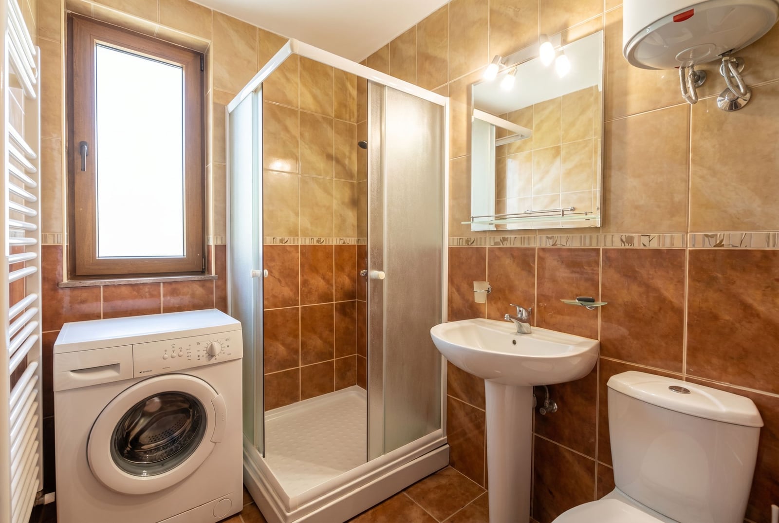Bathroom in a house, Baošići, Montenegro: shower cabin, washing machine, sink, and beige-toned tiles.