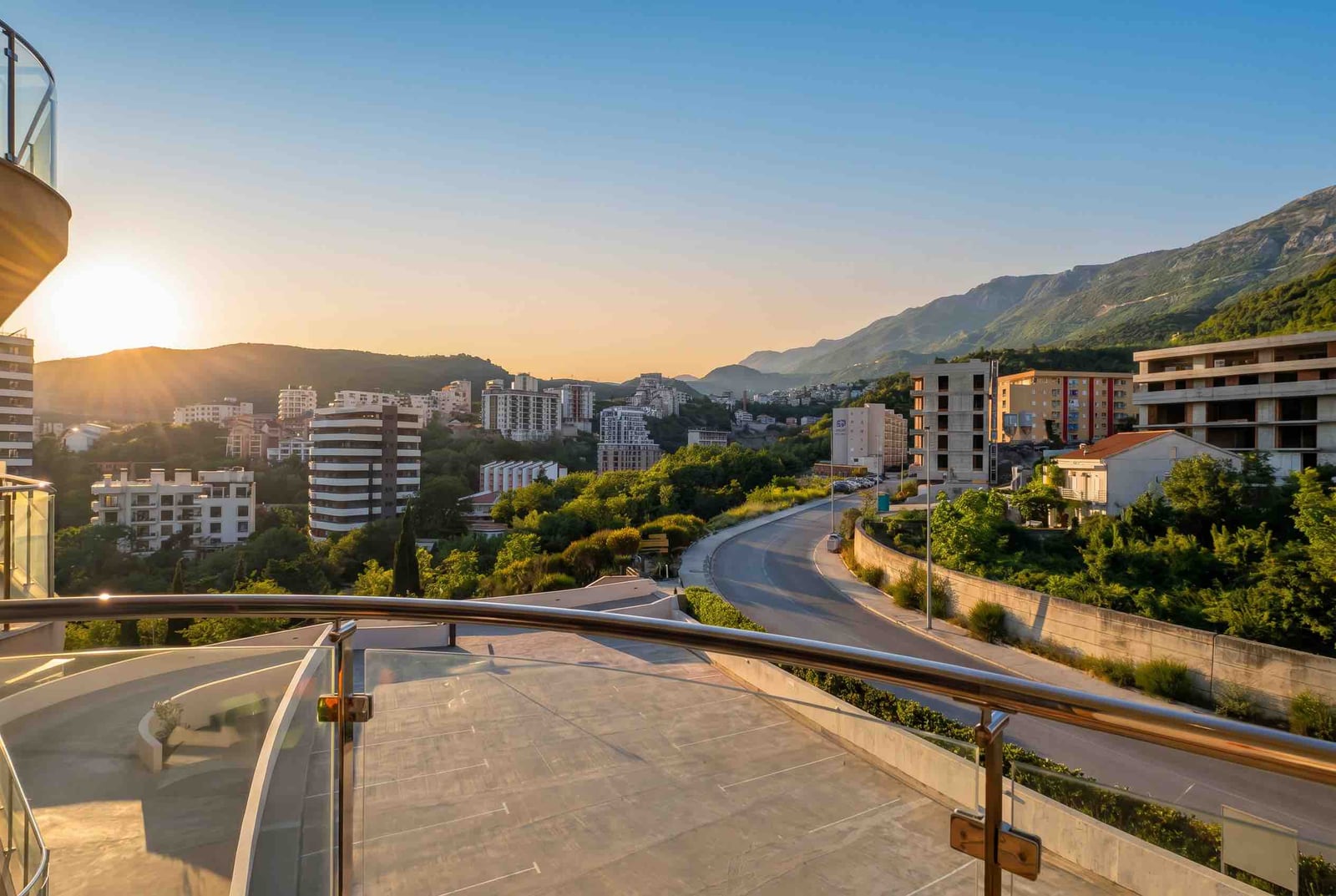 View from the balcony of an apartment in Bečići, Montenegro: city panorama, mountain landscape, and sunset on the horizon.
