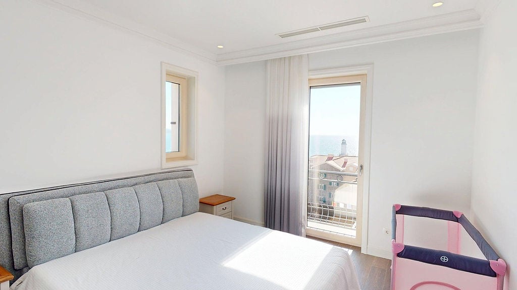 Bright bedroom with a double bed and sea view in the Luštica residential complex, Montenegro. Modern interior with a baby cot.