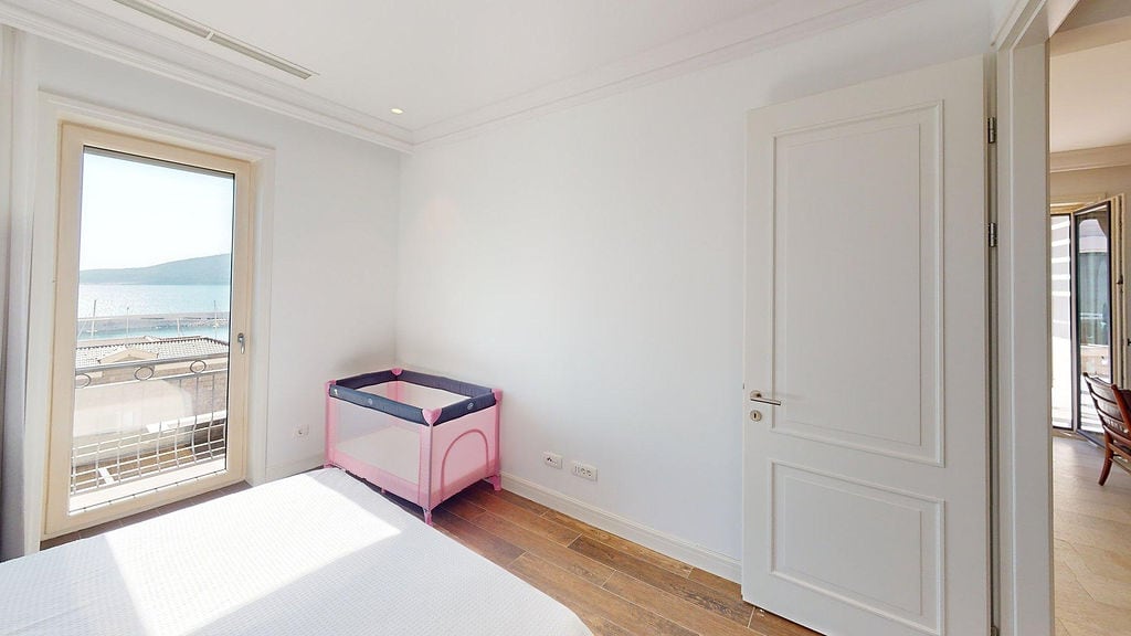 Bright bedroom in an apartment in Luštica, Montenegro, with a baby crib, wooden floor, and a sea view from the window.